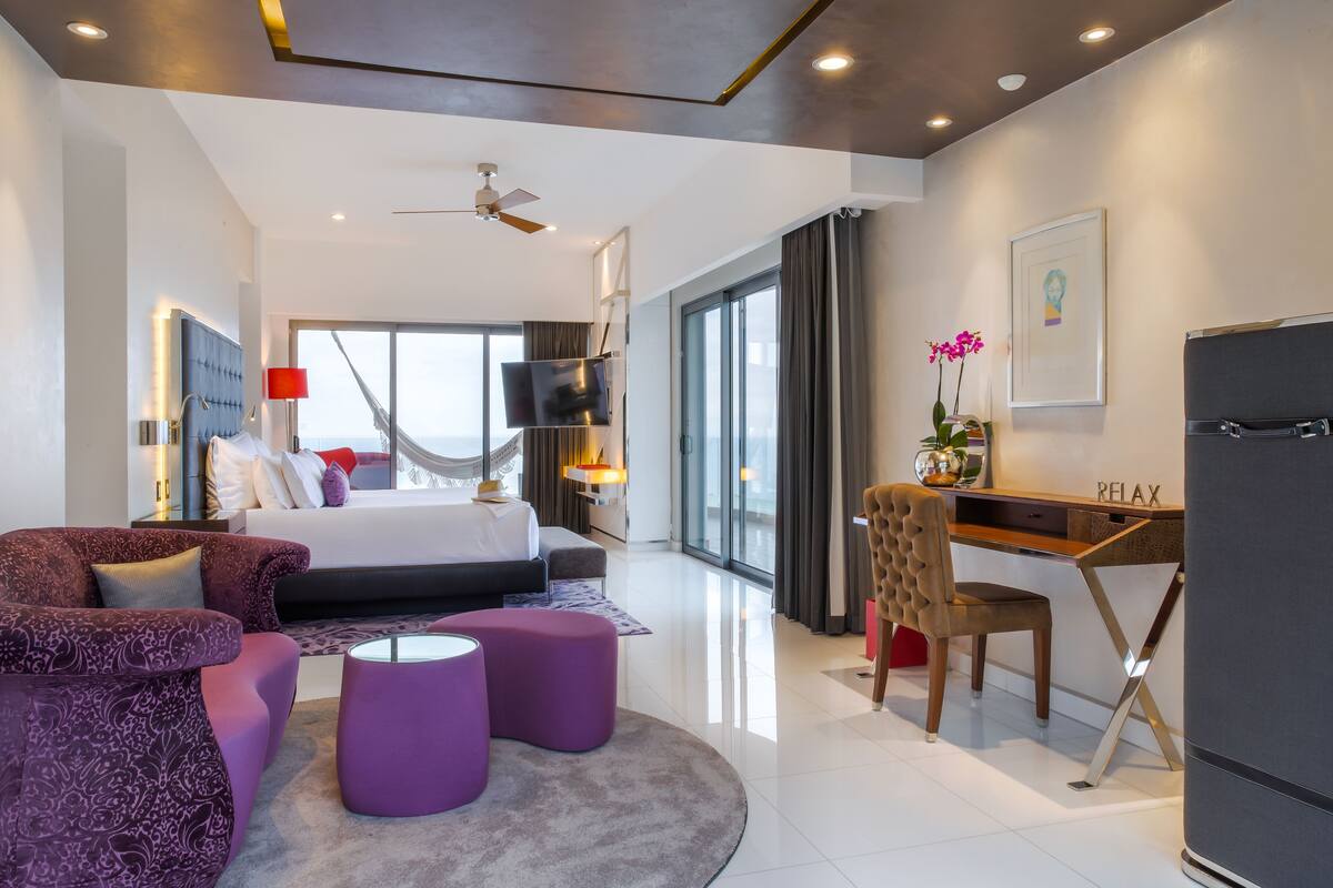 A modern hotel room with a bed, a desk, a chair, and a sofa.