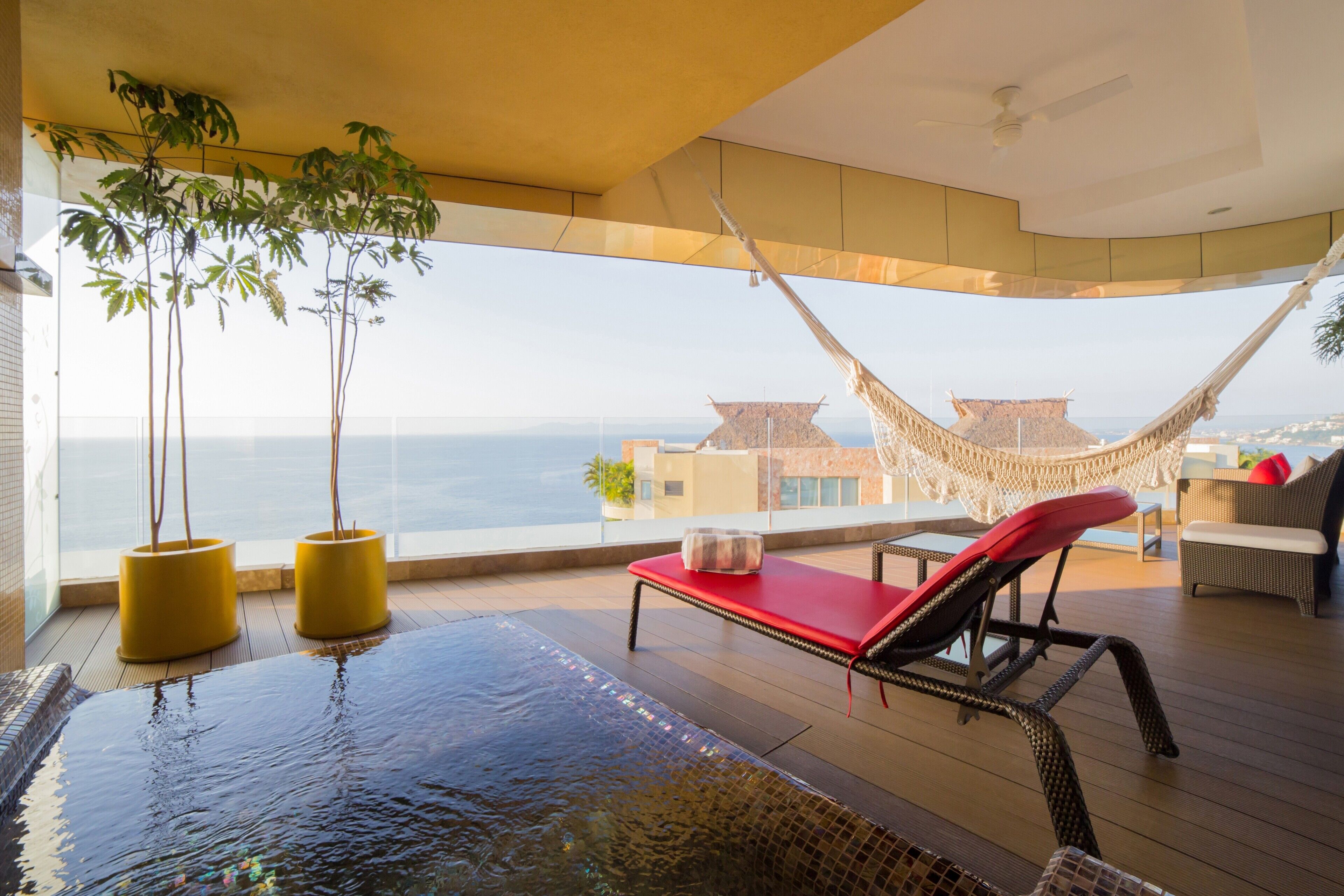 A balcony with a red lounge chair, a hammock, and two potted plants.