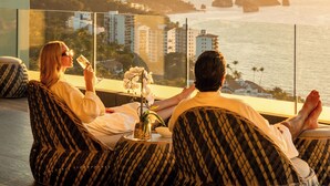 Two people sitting on patterned bean bags with a view of a coastal cityscape and mountains during sunset. - Hotel Mousai Puerto Vallarta Adults Only (Puerto Vallarta)