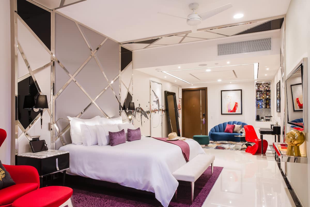 A modern hotel room with a large bed, a desk, a chair, and a sofa.