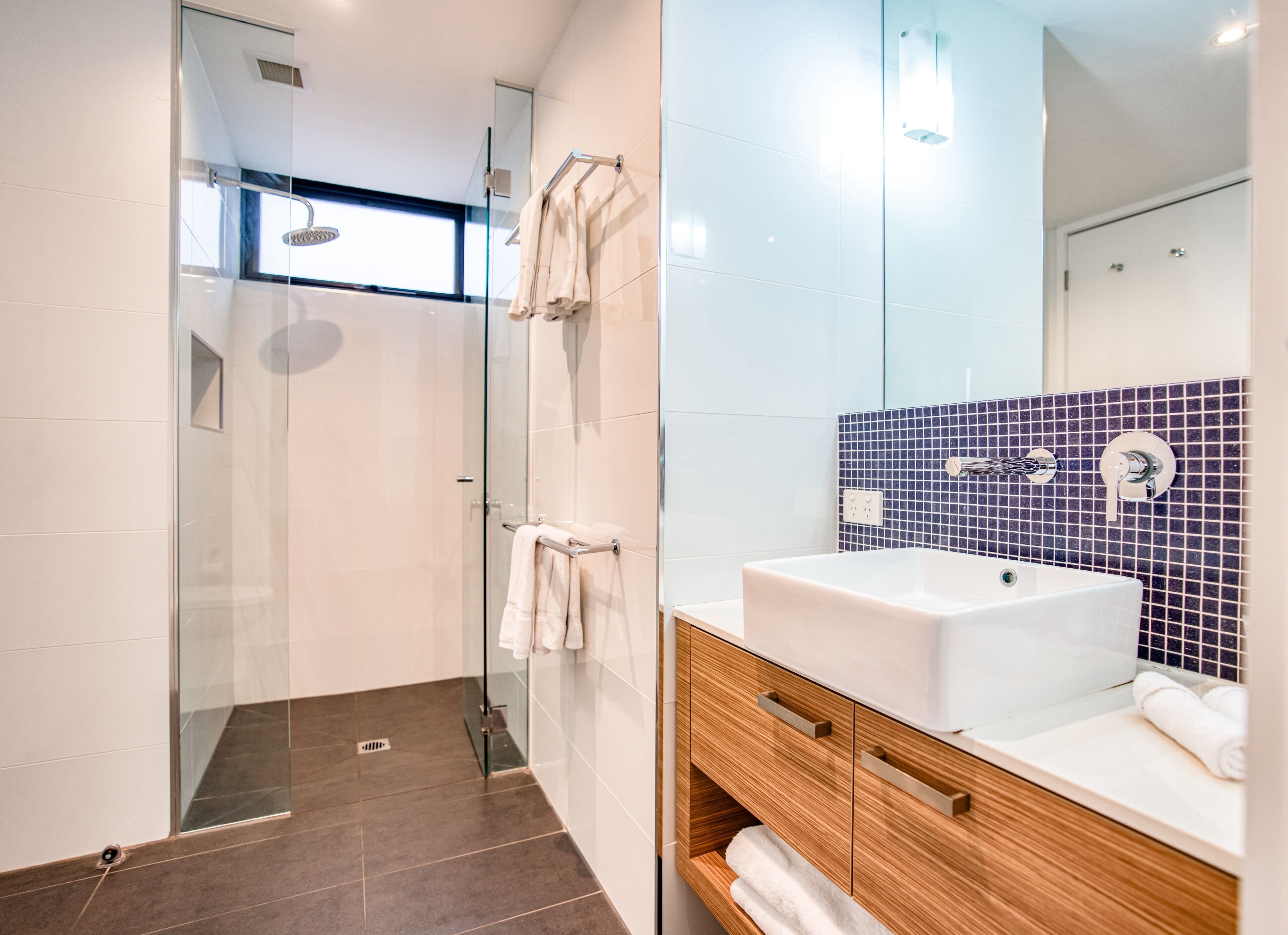 A modern bathroom with a glass-enclosed shower, a white sink, and a wooden vanity.