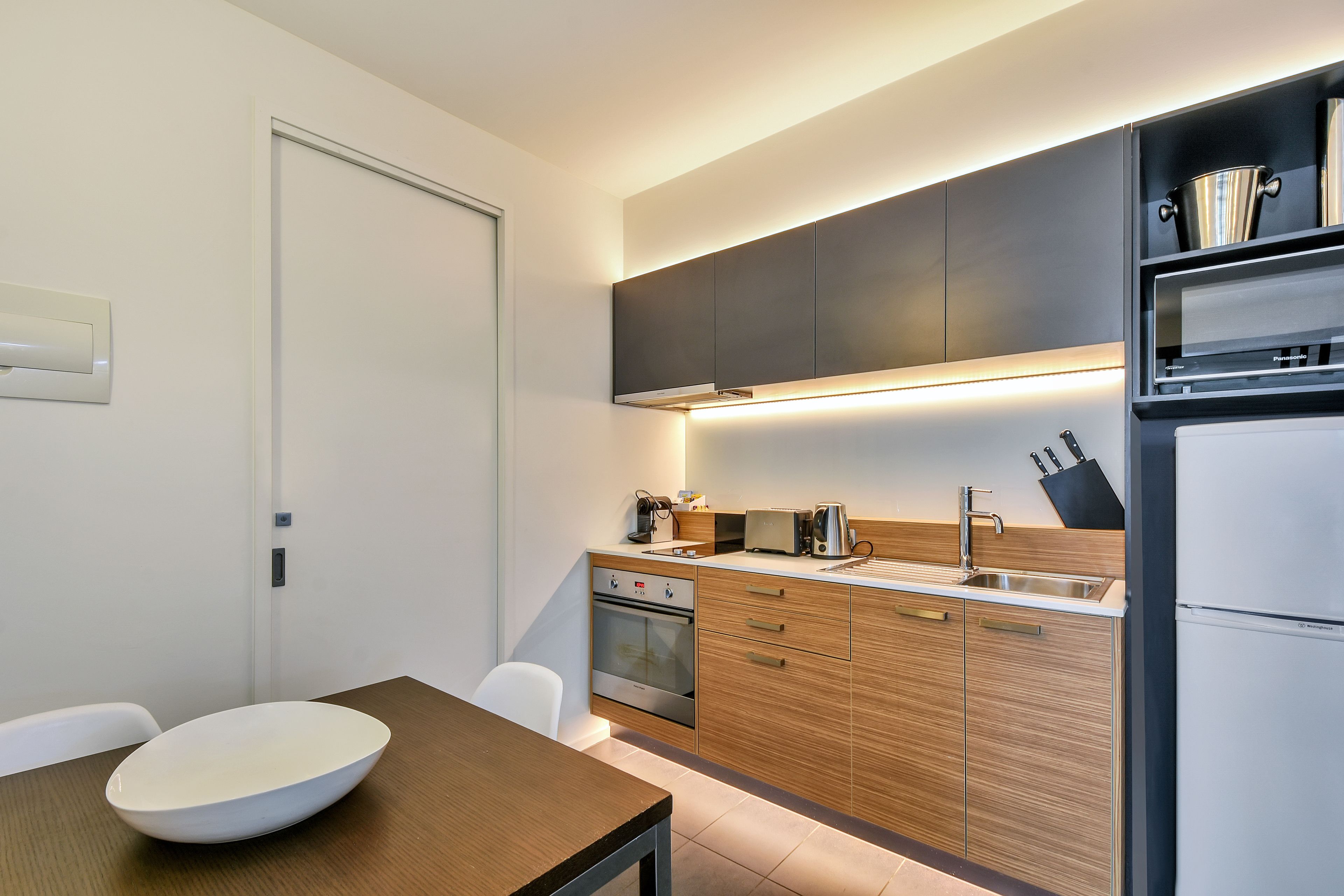 A modern kitchen with wooden cabinets, a built-in oven, a sink, and a white bowl on the table.