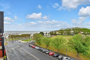 A parking lot with cars, a road, and a view of the ocean and buildings in the distance. - Oaks Vue Suites Geelong (Geelong)