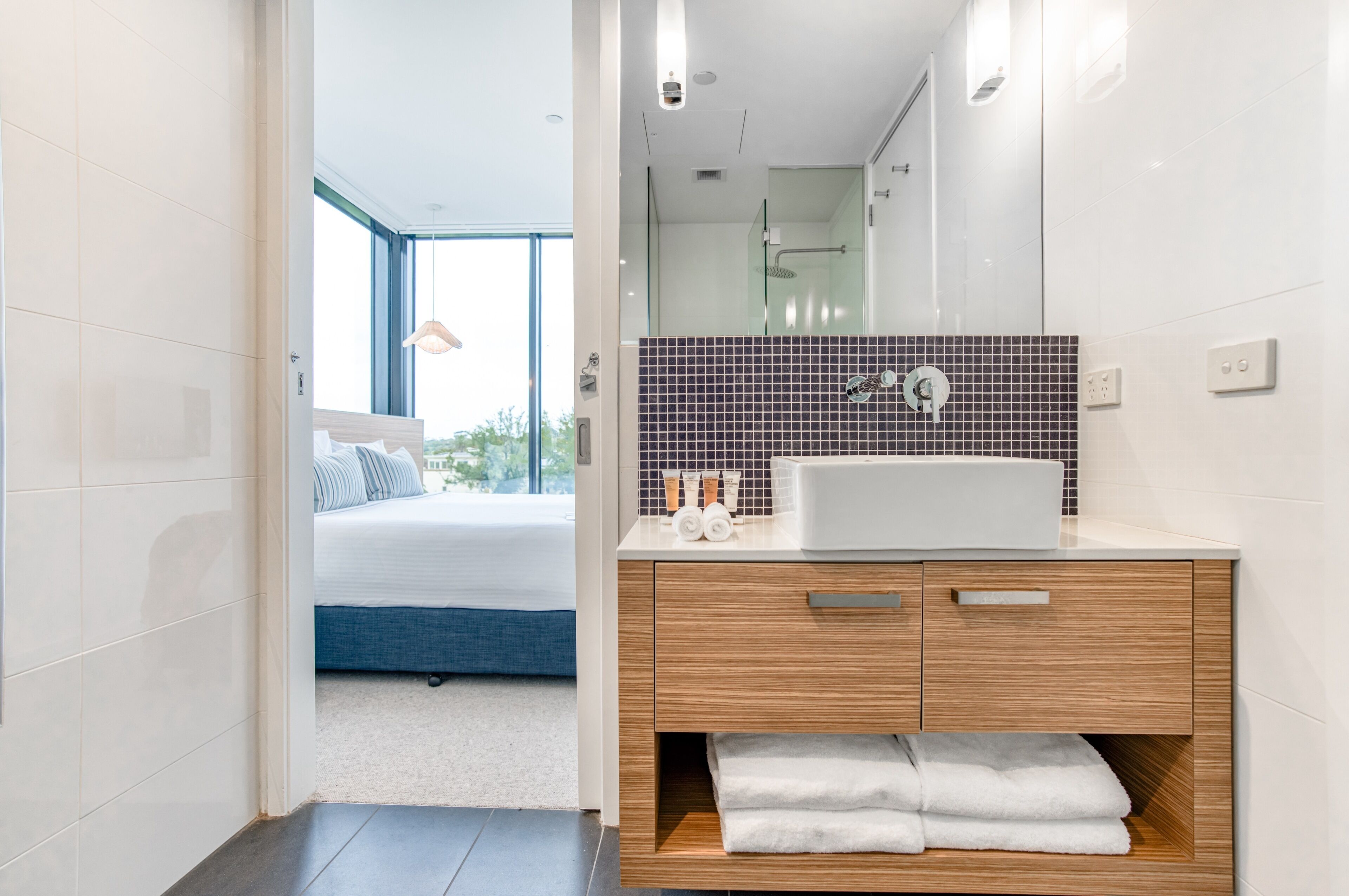 Un baño moderno con un espejo grande, un lavamanos blanco y un mueble de tocador de madera.