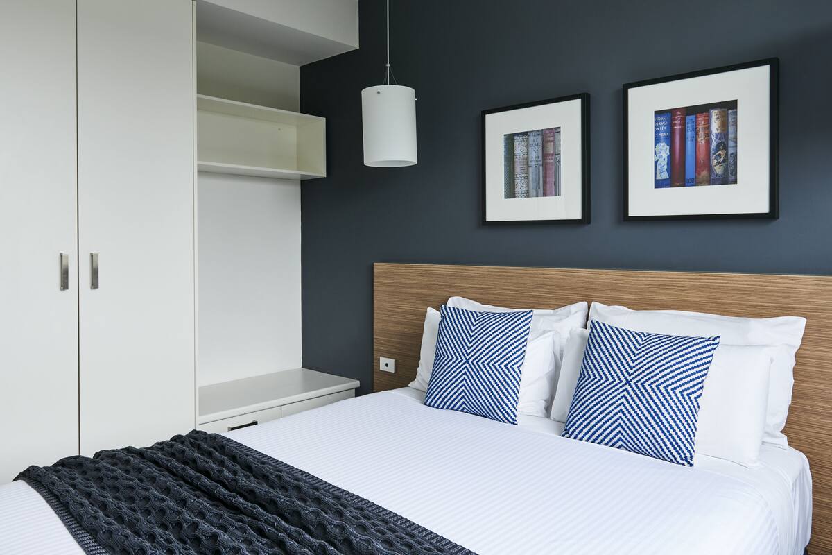 A modern bedroom with a bed, white wardrobe, and two framed books on the wall.