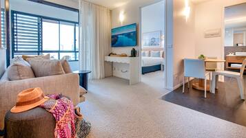 A modern hotel room with a sofa, a dining area, a bed, and a TV.