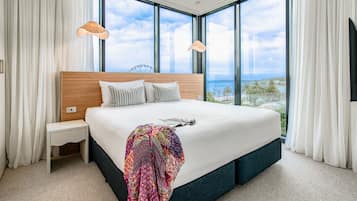 A modern bedroom with a large bed, a nightstand, and a view of the sea through large windows.