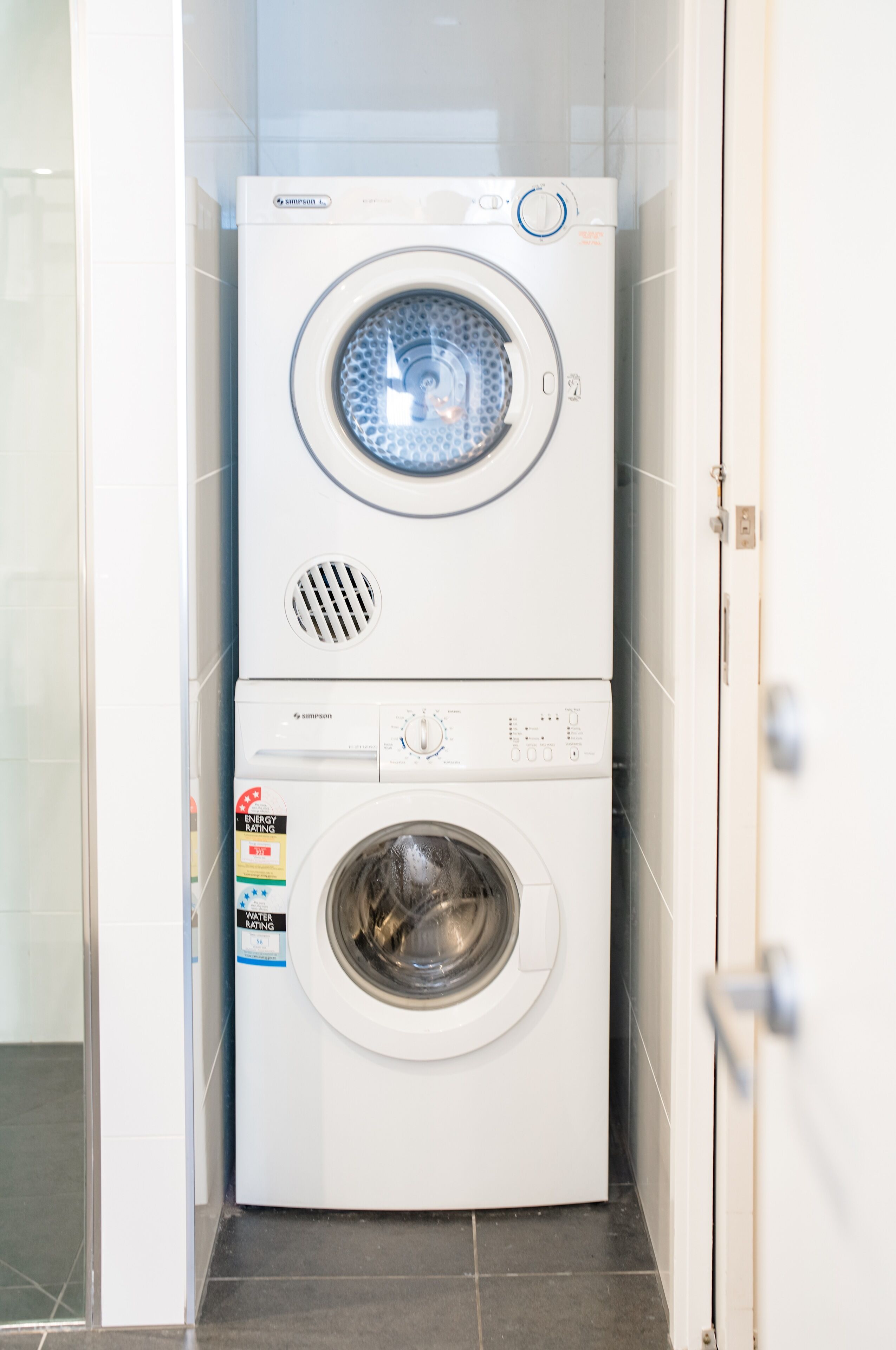 A stacked washer and dryer unit in a bathroom with tiled walls and floor.