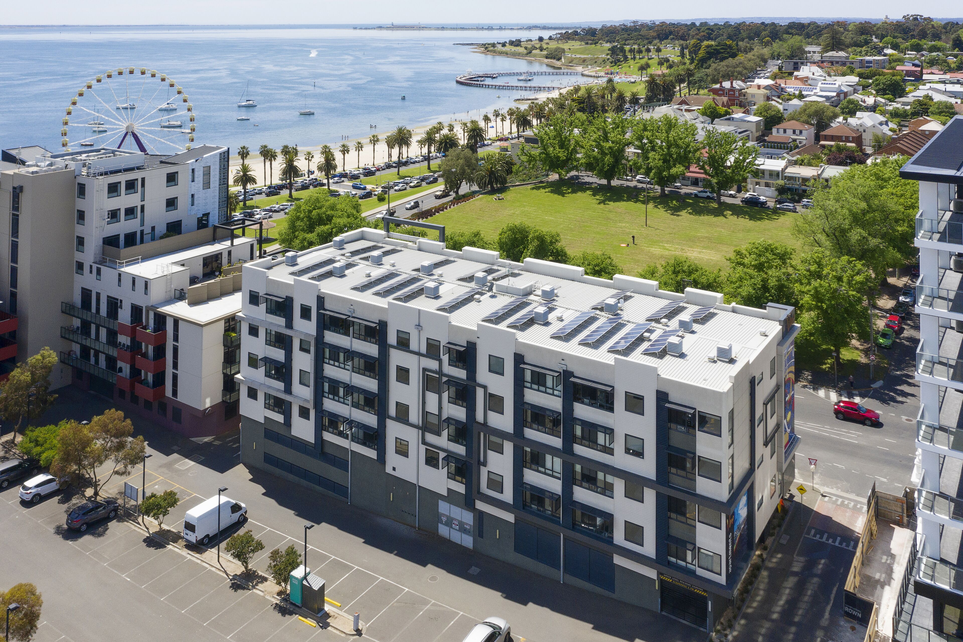 A modern multi-story building with a flat roof, large windows, and a parking lot.