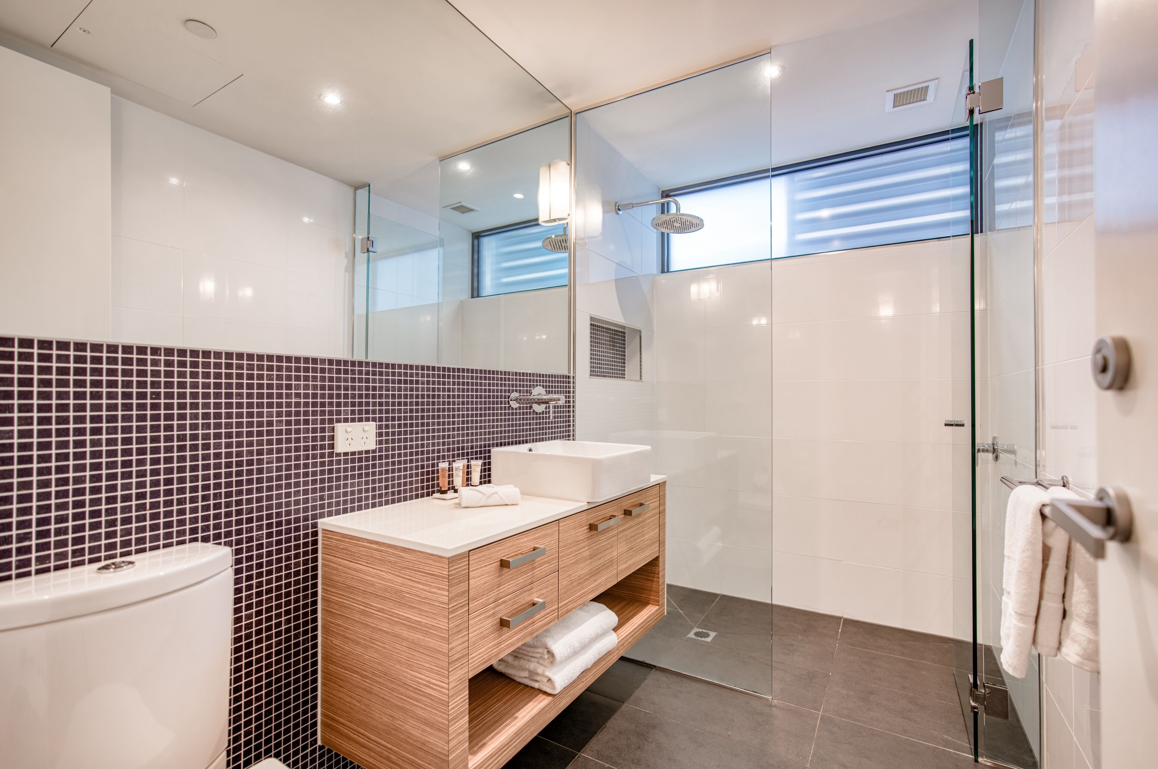 A modern bathroom with a glass shower enclosure, a wooden vanity with a sink, and a tiled backsplash.