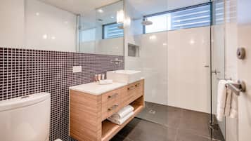 A modern bathroom with a glass shower enclosure, a wooden vanity with a sink, and a tiled backsplash.