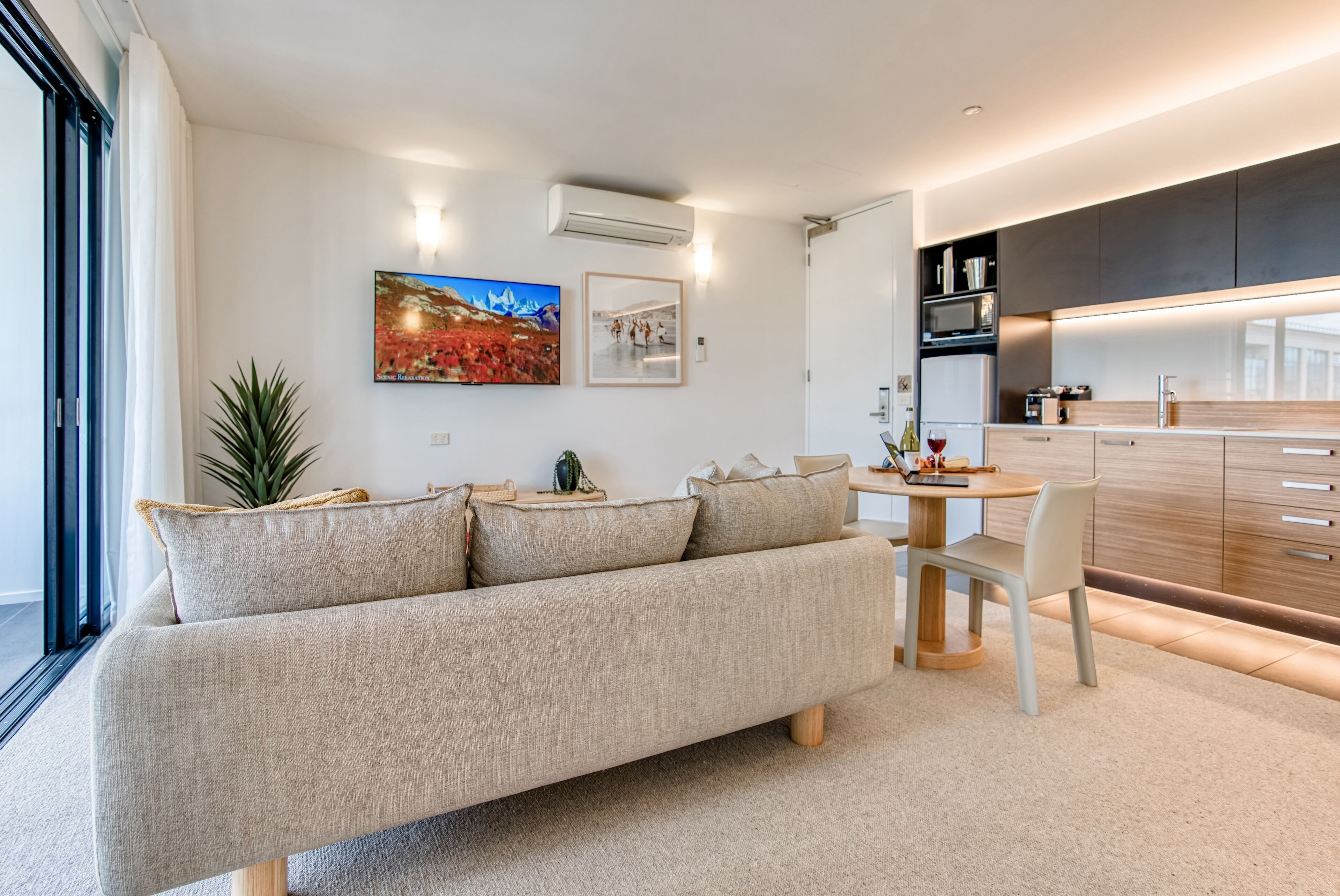 A modern living room with a sofa, a dining table, and a kitchen area.
