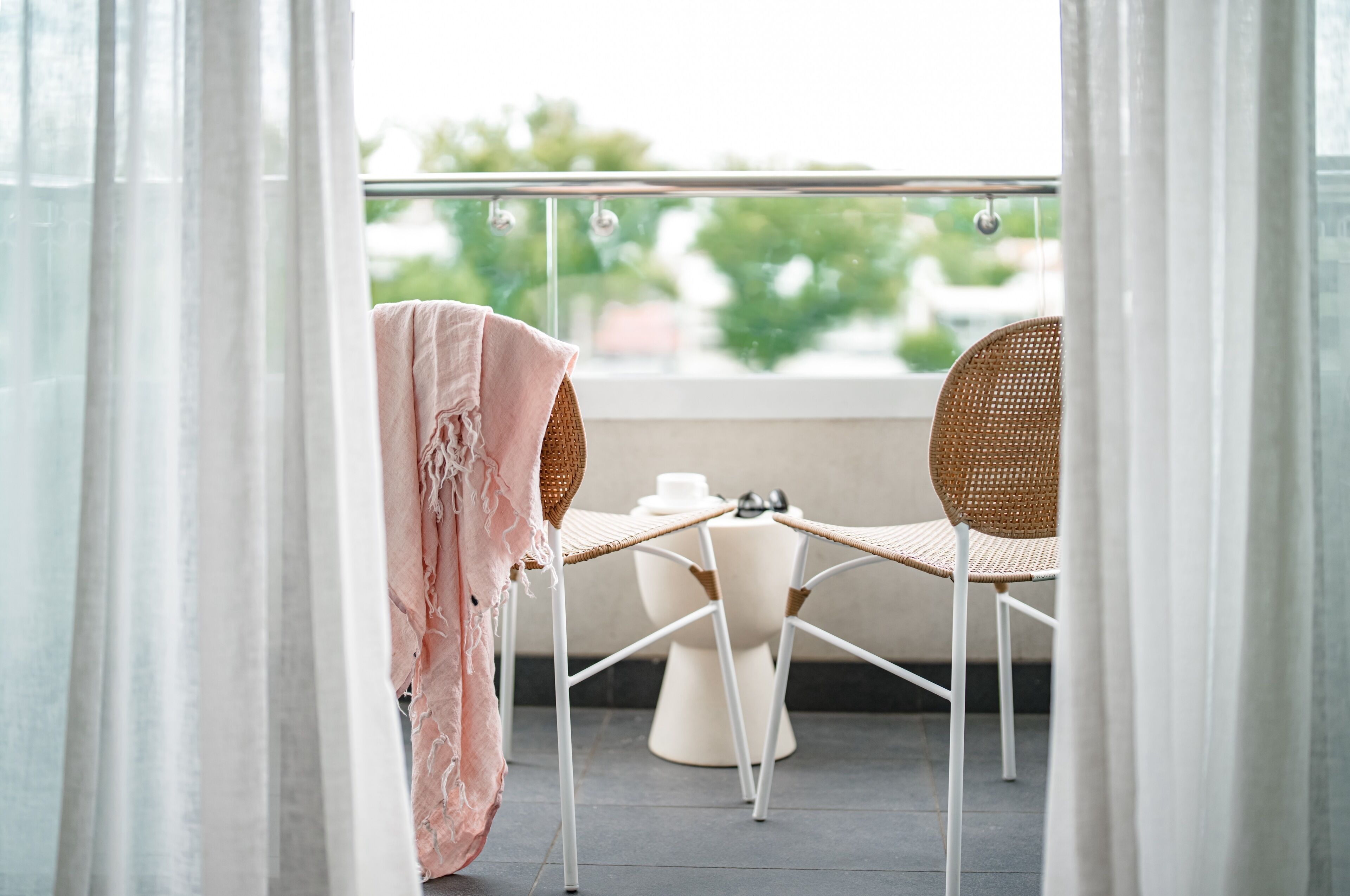 A balcony with two wicker chairs, a small table, and a white pedestal.
