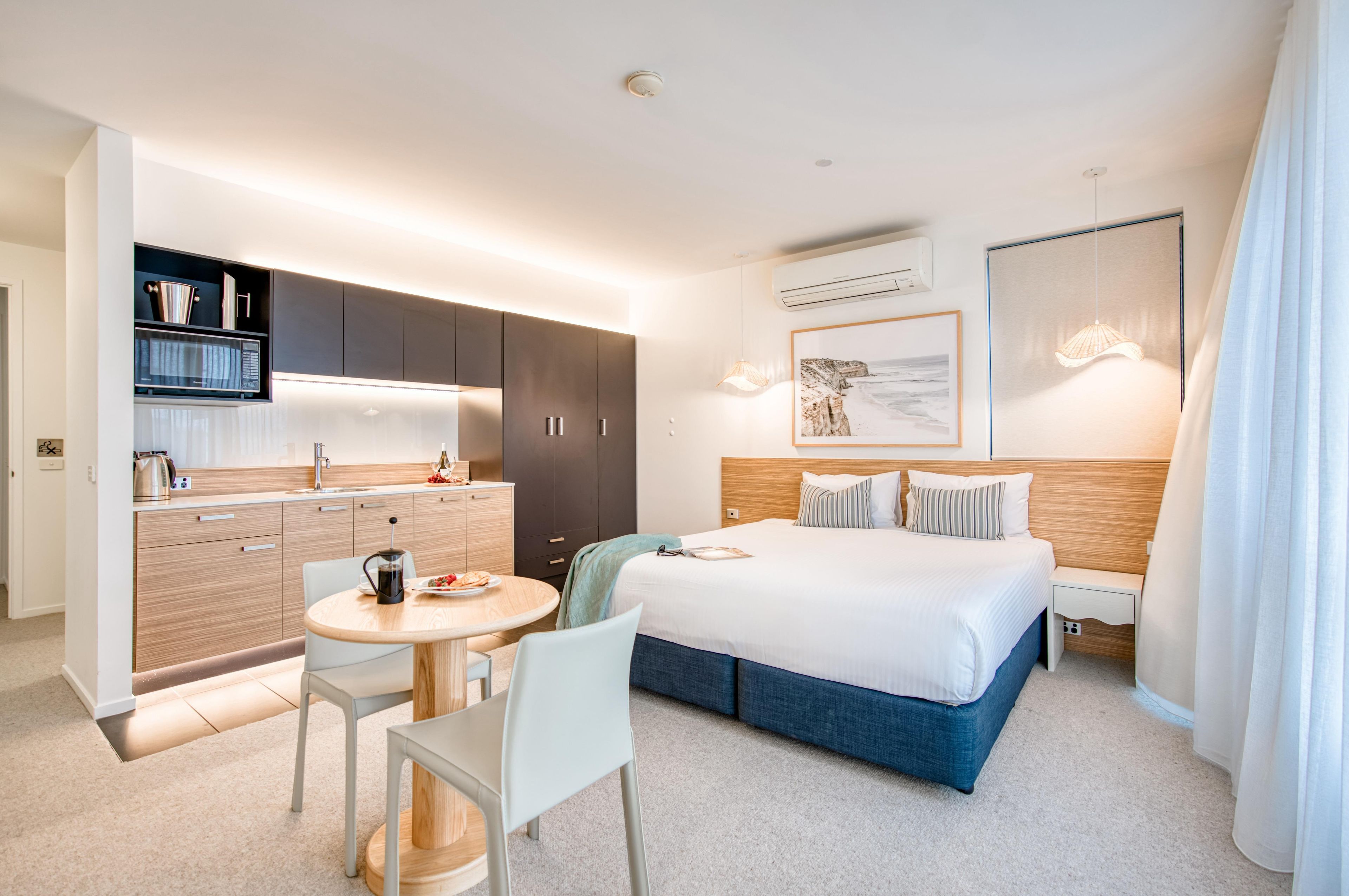 A modern hotel room with a bed, bedside table, and a small kitchen area with a coffee maker and a kettle.