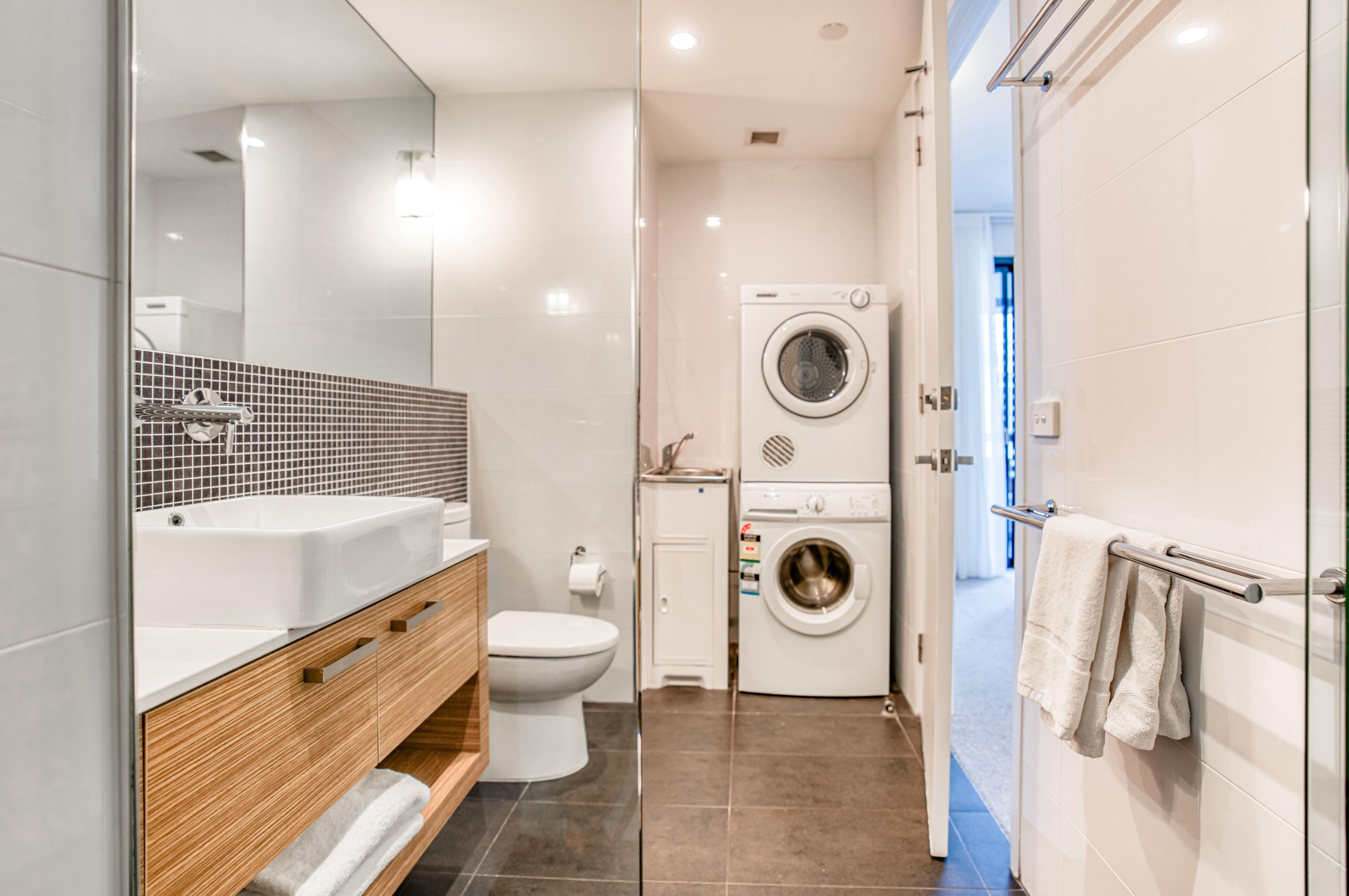 A modern bathroom with a large mirror, a sink, a toilet, a washing machine, and a shower area.