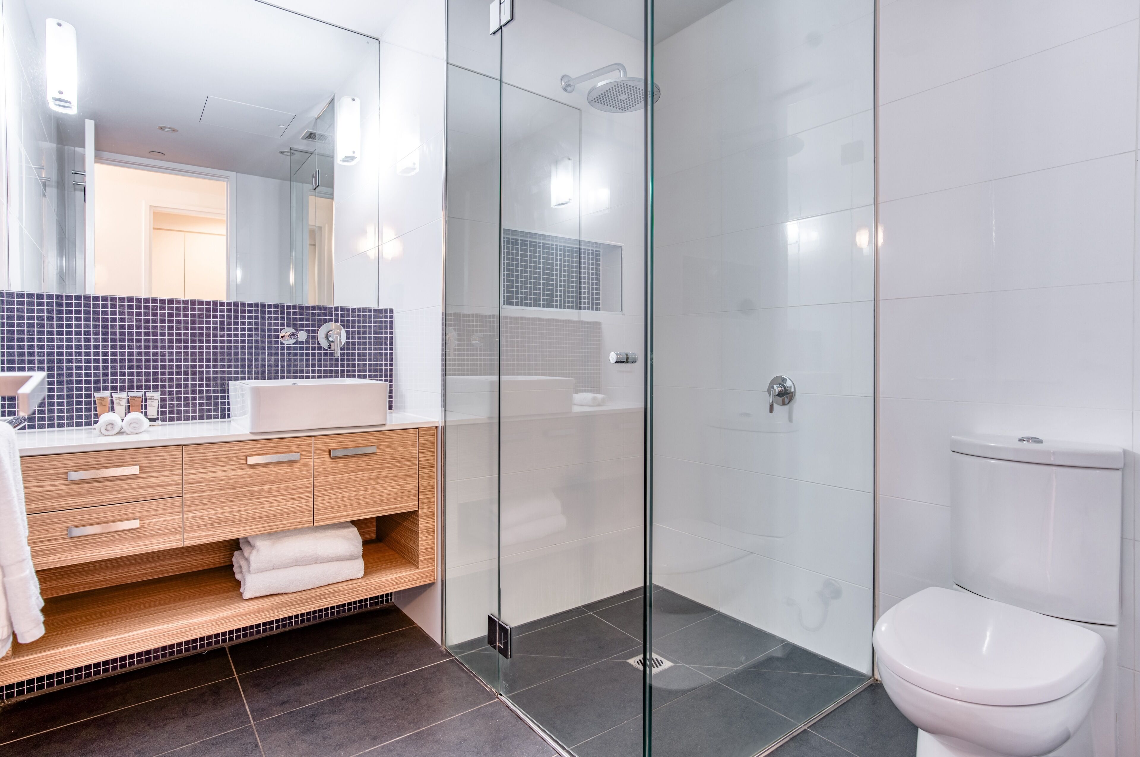 Een moderne badkamer met een douchecabine van glas, een wit toilet en een wastafel met spiegel en handdoekhouder.