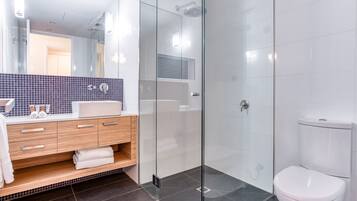 Een moderne badkamer met een douchecabine van glas, een wit toilet en een wastafel met spiegel en handdoekhouder.