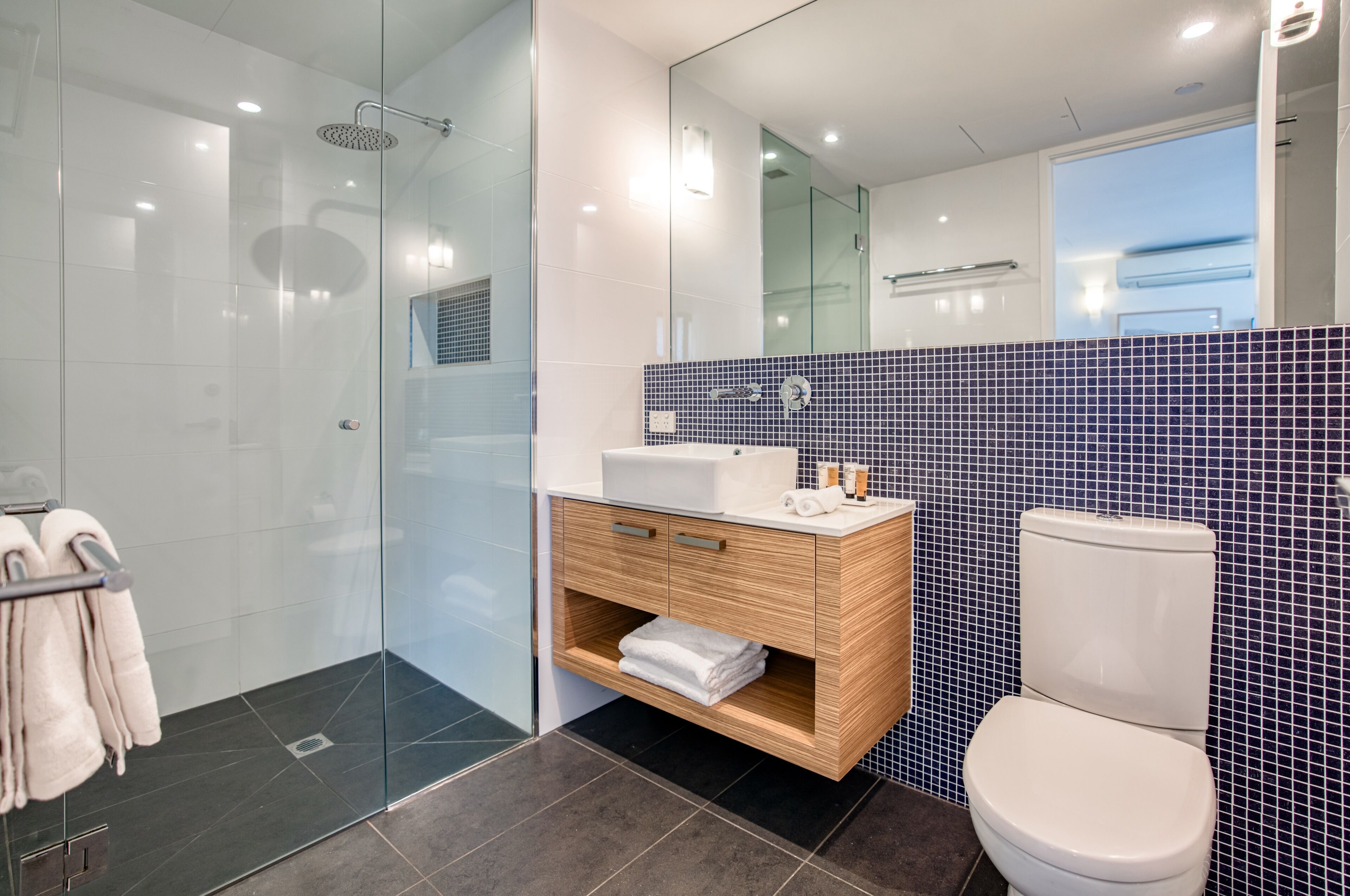Et moderne badeværelse med glasbrusekabine, et trækommode med vask og et toilet.
