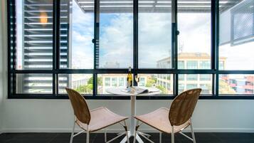 A room with a large window, two wicker chairs, a small table, and a bottle of wine.