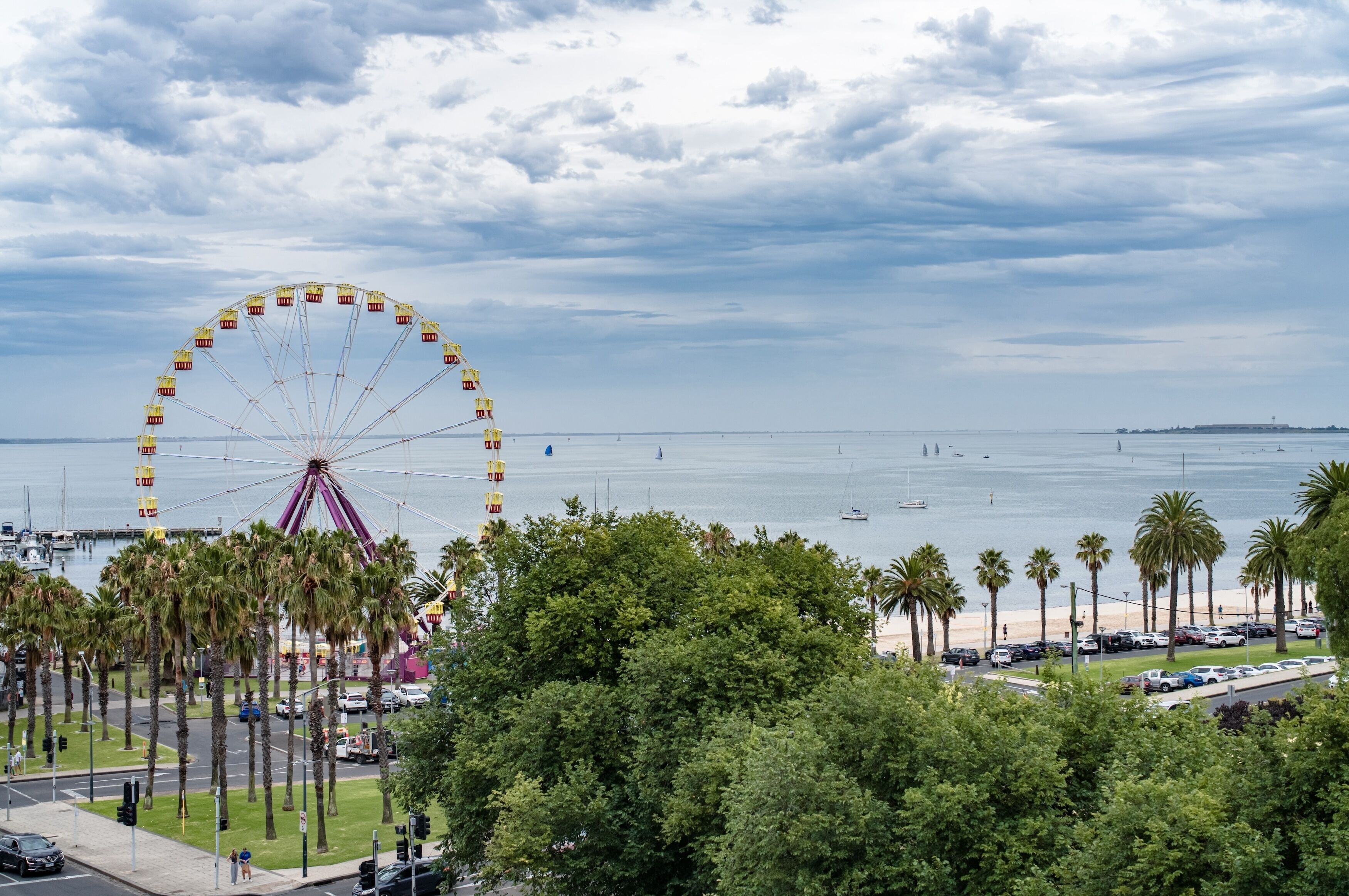 A coastal view with a large Ferris wheel, palm trees, and a marina.