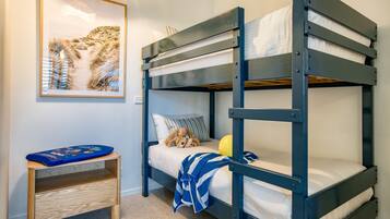 A bunk bed with a teddy bear and a ball, a small wooden table, and a framed picture on the wall.