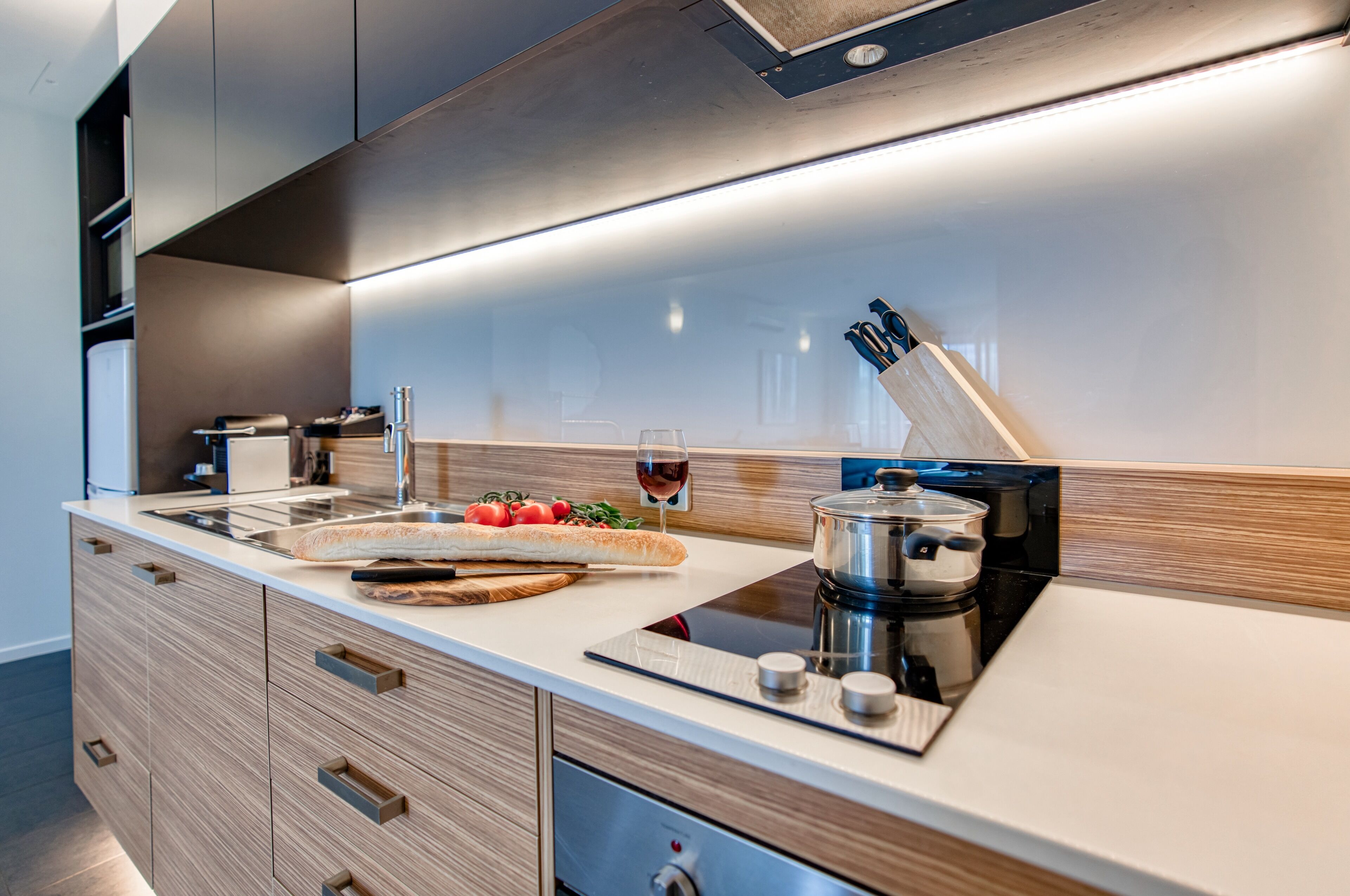 A modern kitchen with a built-in stove, a cutting board with vegetables, and a glass of red wine.