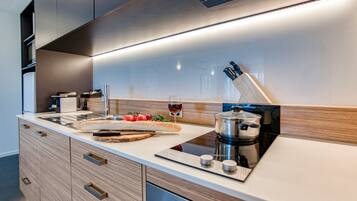 A modern kitchen with a built-in stove, a cutting board with vegetables, and a glass of red wine.