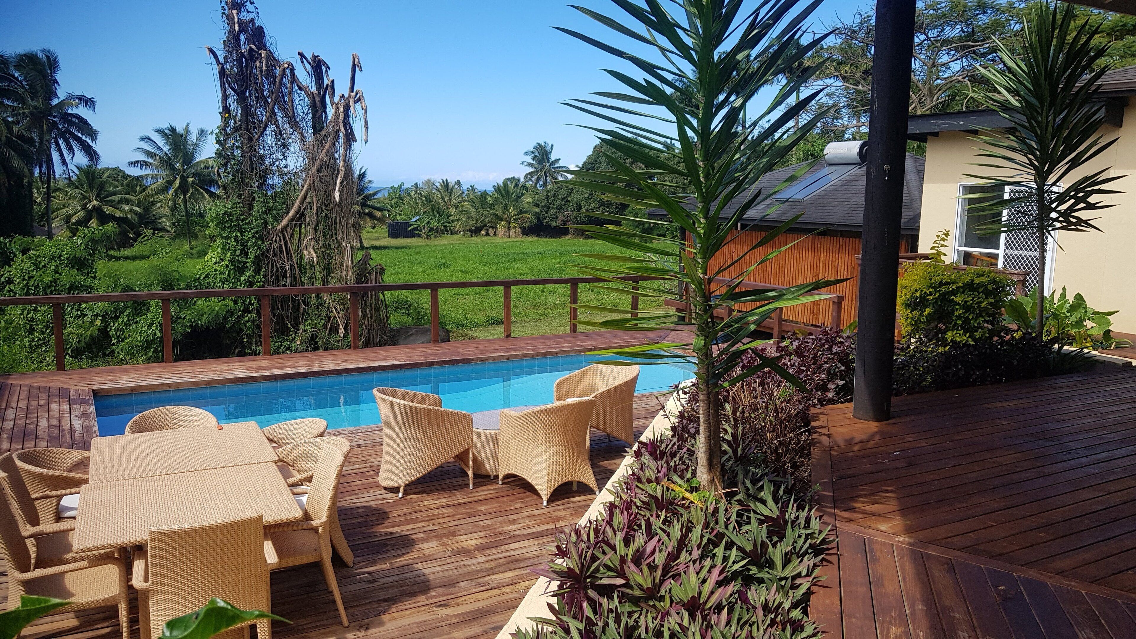 A pool area with wicker furniture and a view of a green landscape.