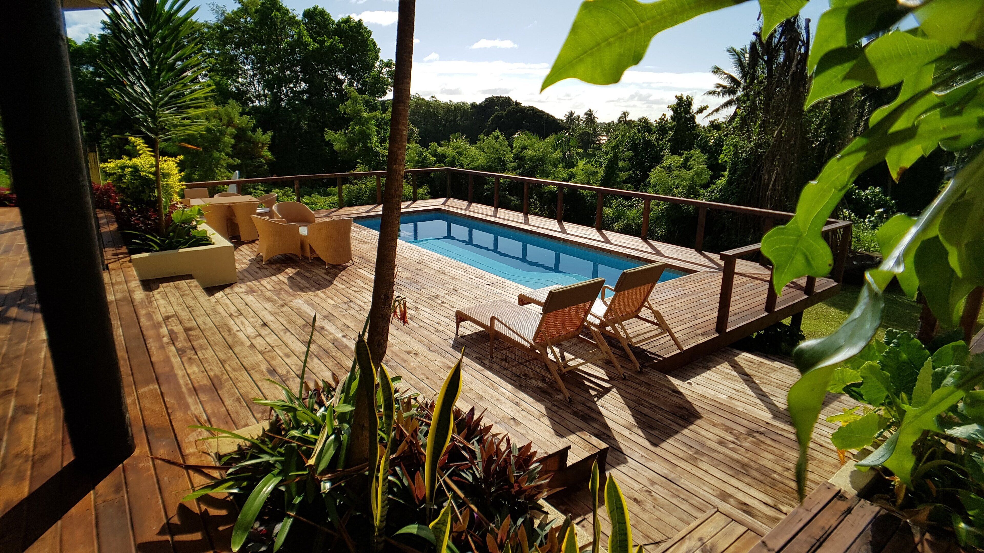 A wooden deck with a pool, surrounded by lush greenery and trees.