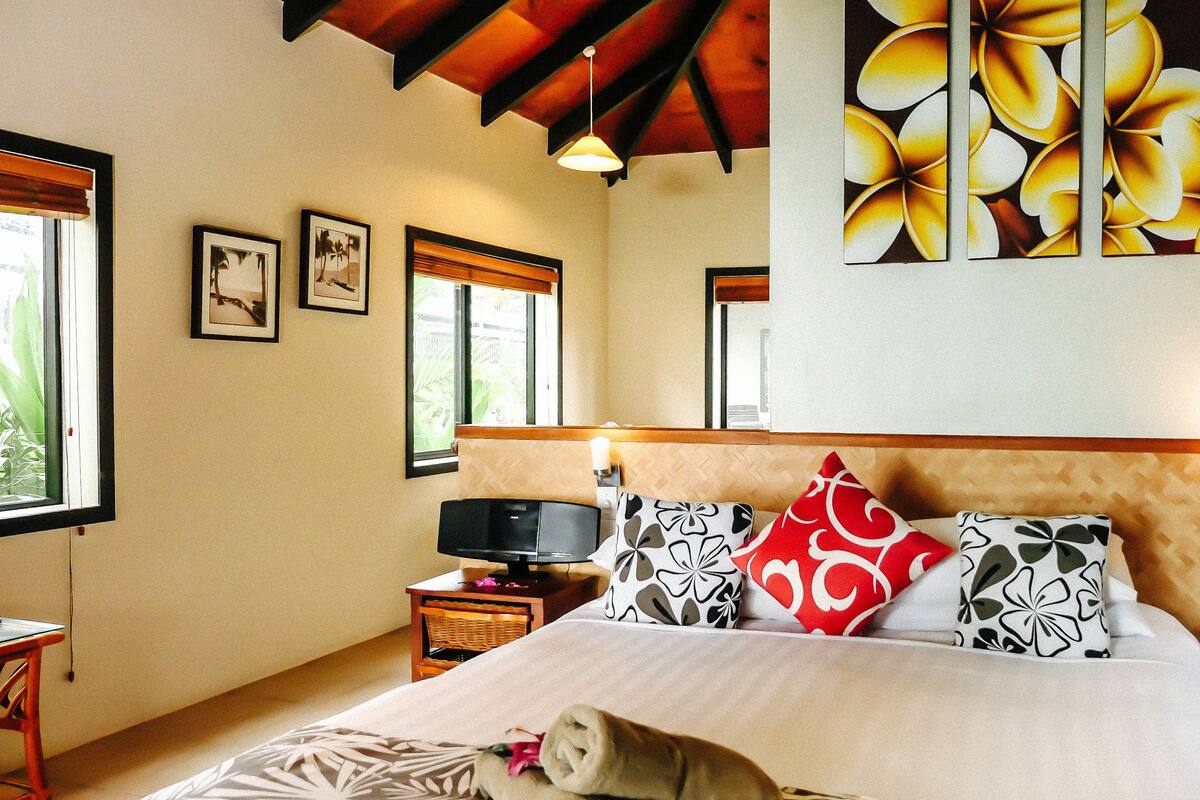 Un dormitorio con cama, almohadas, televisión y una obra de arte en la pared.