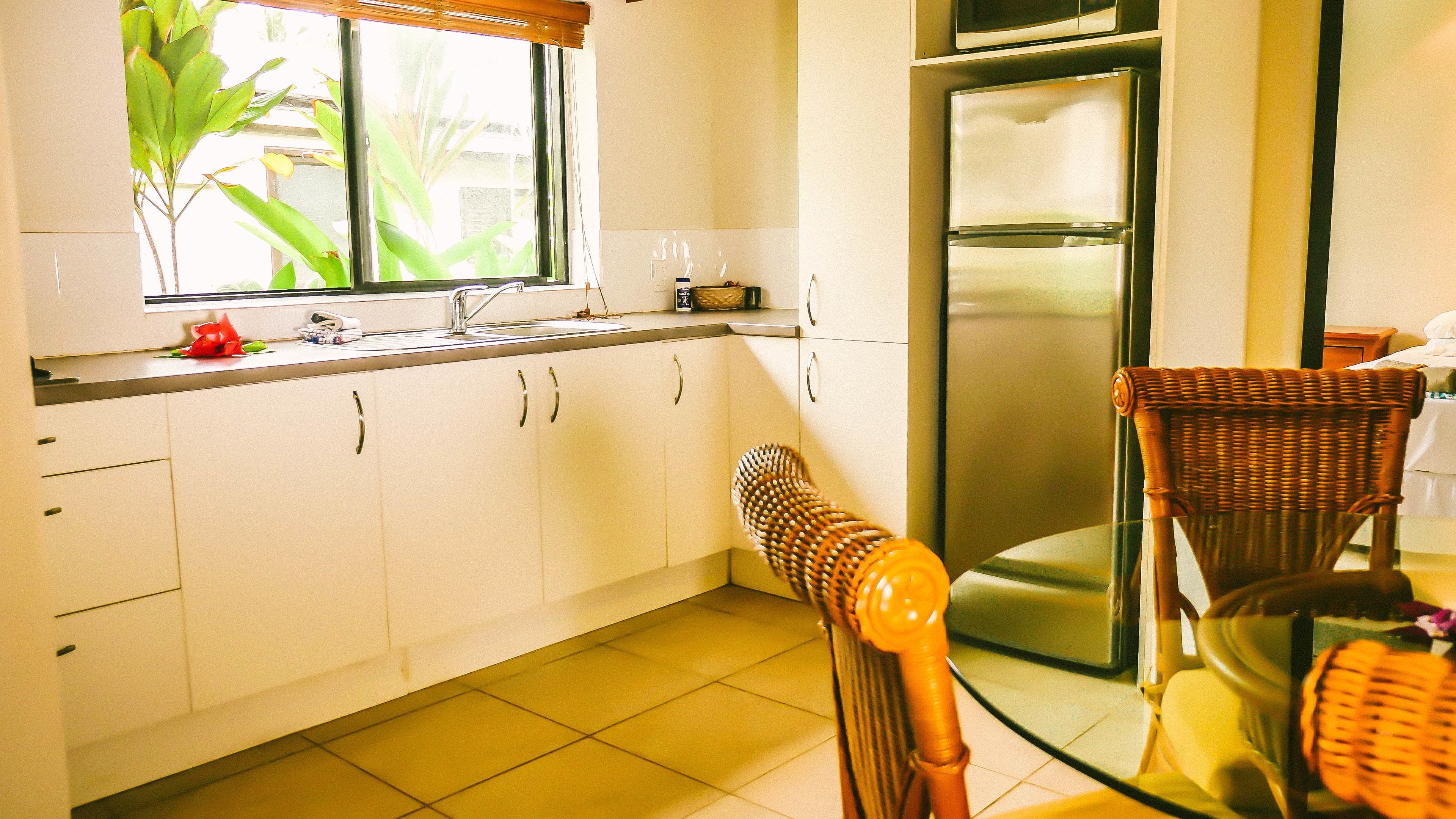 A kitchen with white cabinets, a stainless steel refrigerator, a sink, and a window with plants.