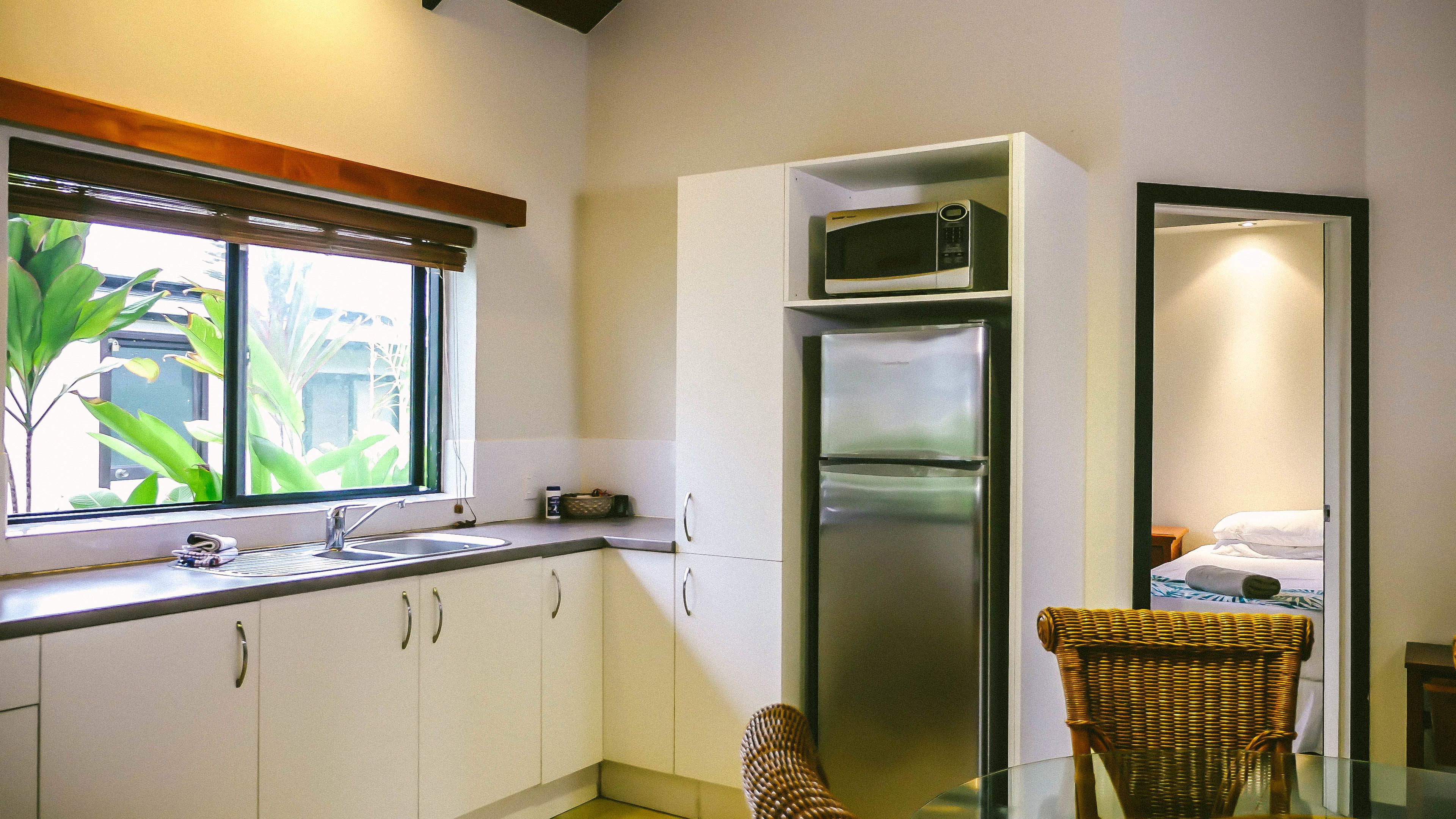 A compact kitchen with a built-in microwave, a stainless steel refrigerator, and a window with blinds.
