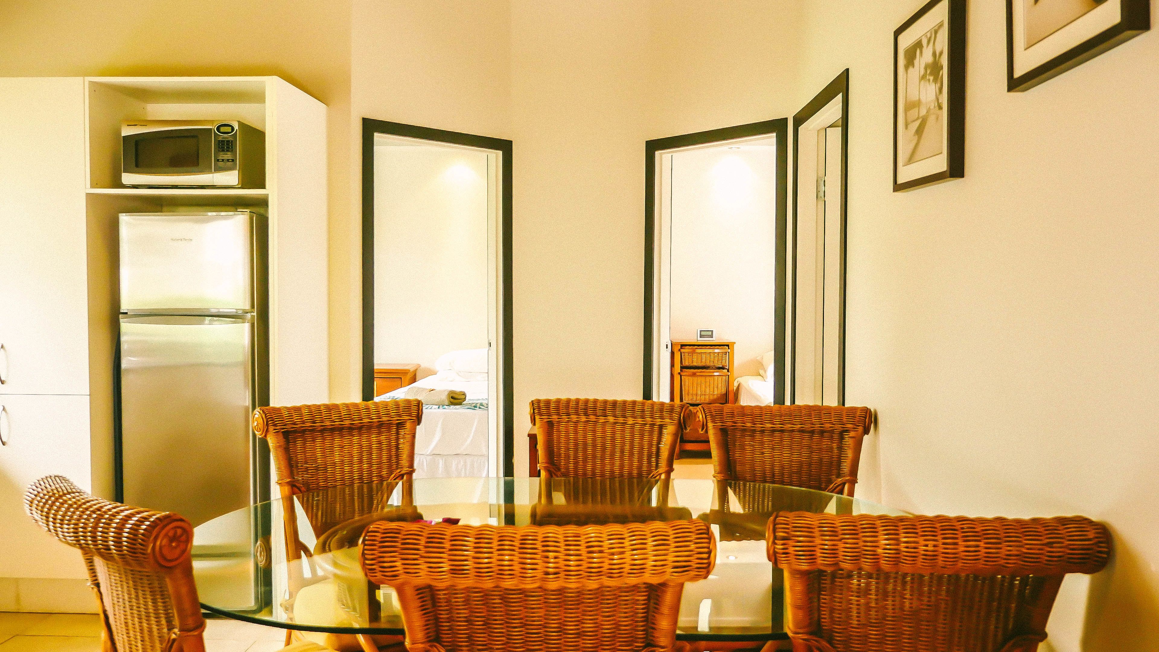 A dining area with a glass table surrounded by wicker chairs, a refrigerator, and a microwave on the left.