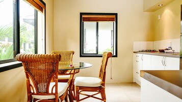 A compact kitchen with a dining area, featuring wicker chairs, a glass table, and a window with a view of greenery.