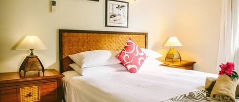 A neatly made bed with white linens, a red and white pillow, and a patterned throw. There are two bedside lamps and a wall-mounted light fixture.