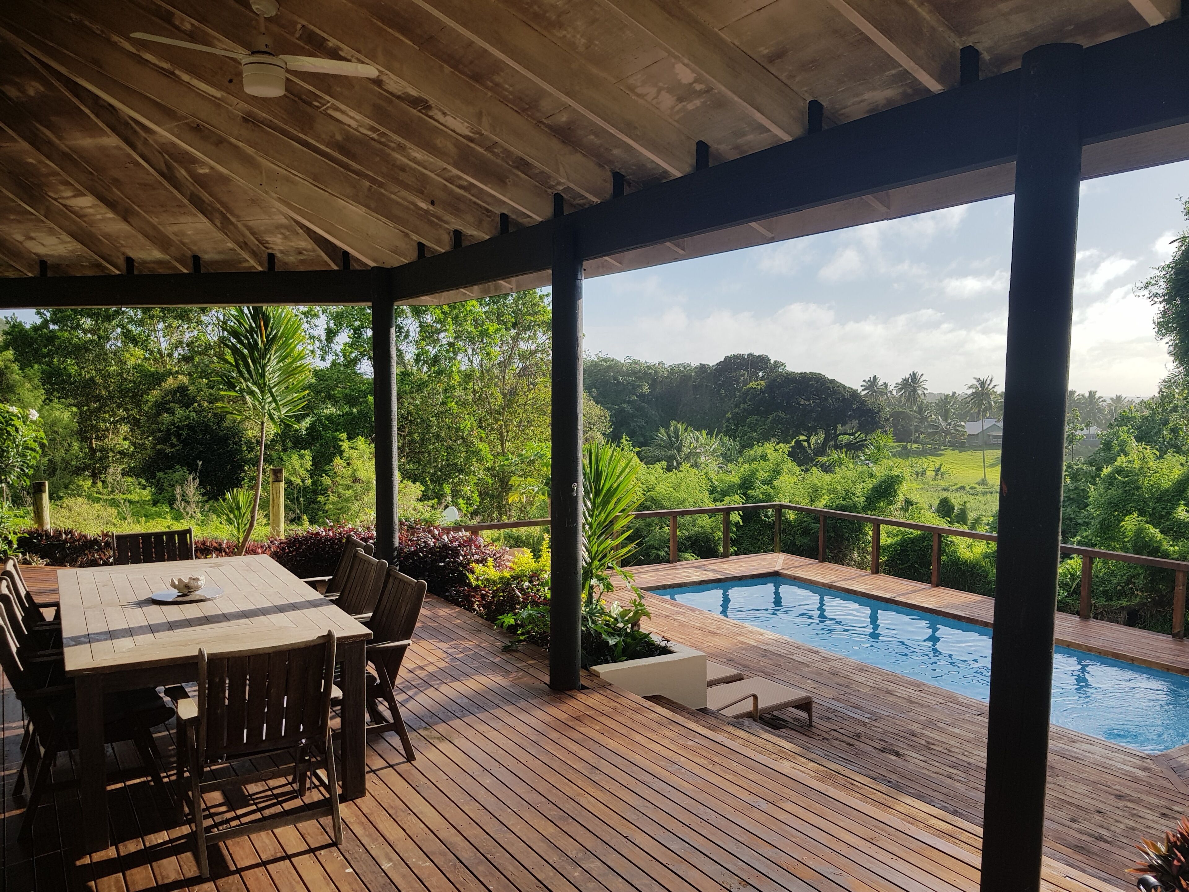 A covered outdoor area with a pool, wooden deck, and seating.
