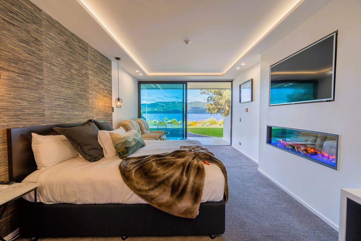 Een moderne slaapkamer met een groot bed, een open haard, een televisie en uitzicht op de natuur.