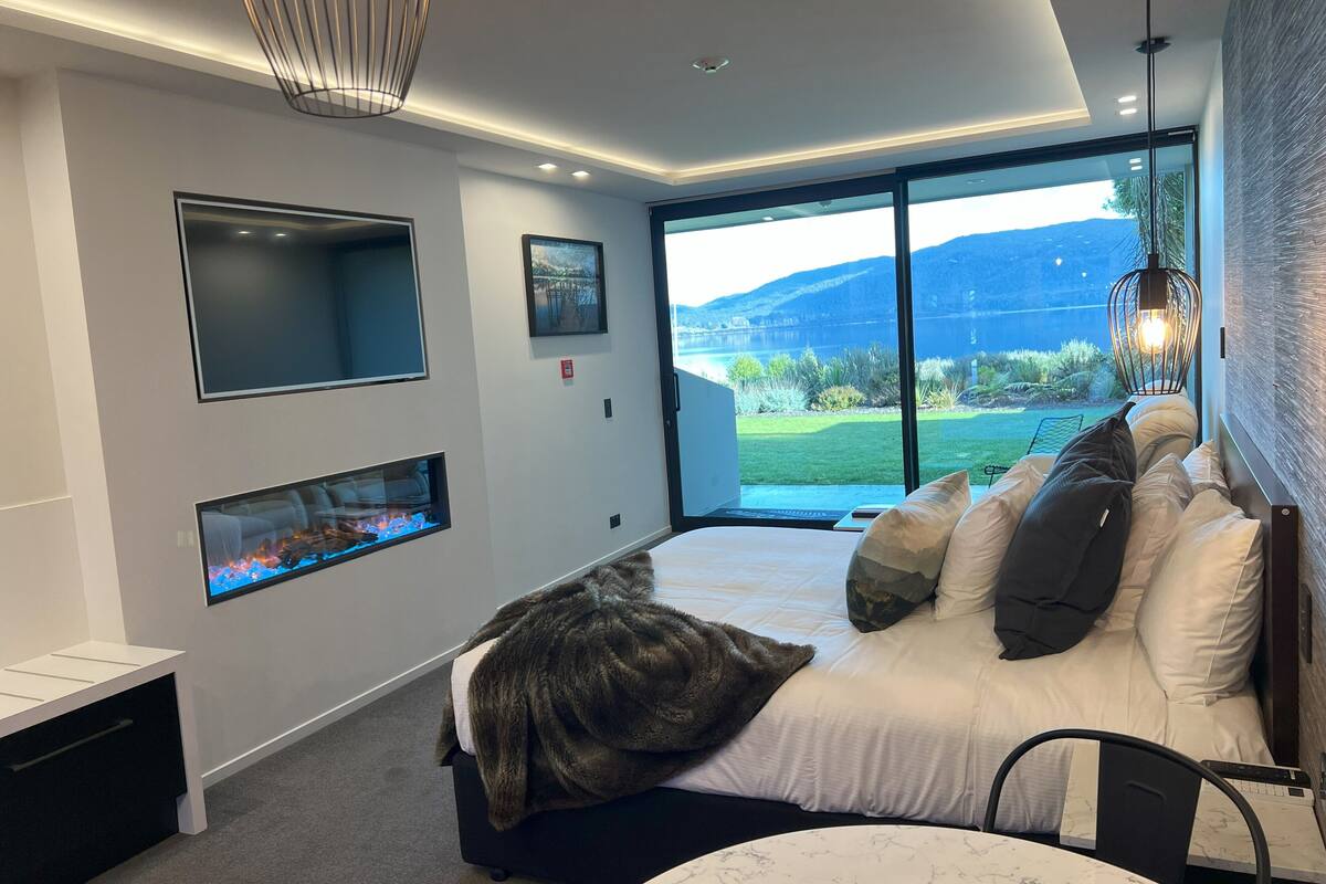Une chambre moderne avec un grand lit, une cheminée, une télévision et une vue sur une montagne et un lac.