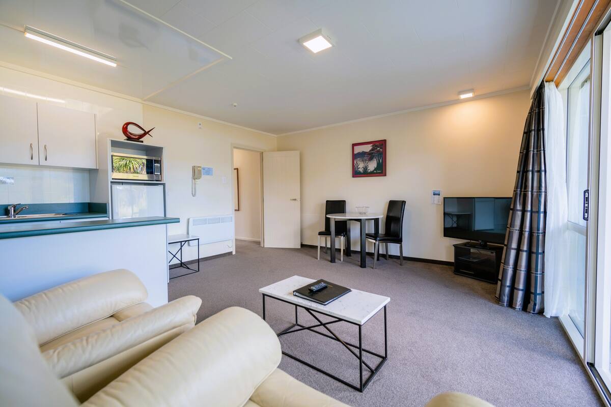 Een moderne woonkamer met een bank, salontafel, televisie, en een keukenhoek met een magnetron en koelkast.
