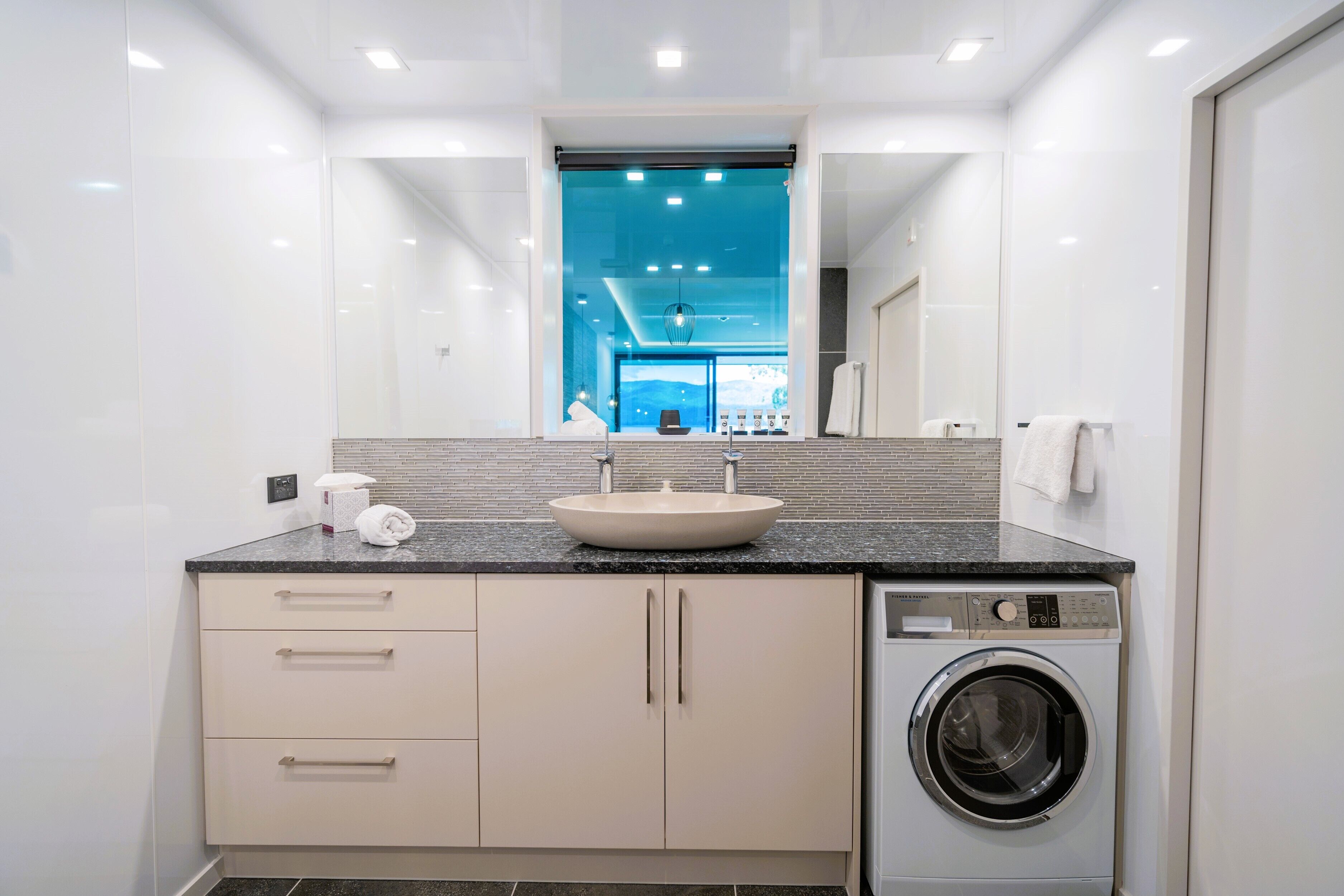Une salle de bain moderne équipée d’un lavabo, d’un miroir et d’un lave-linge encastré.