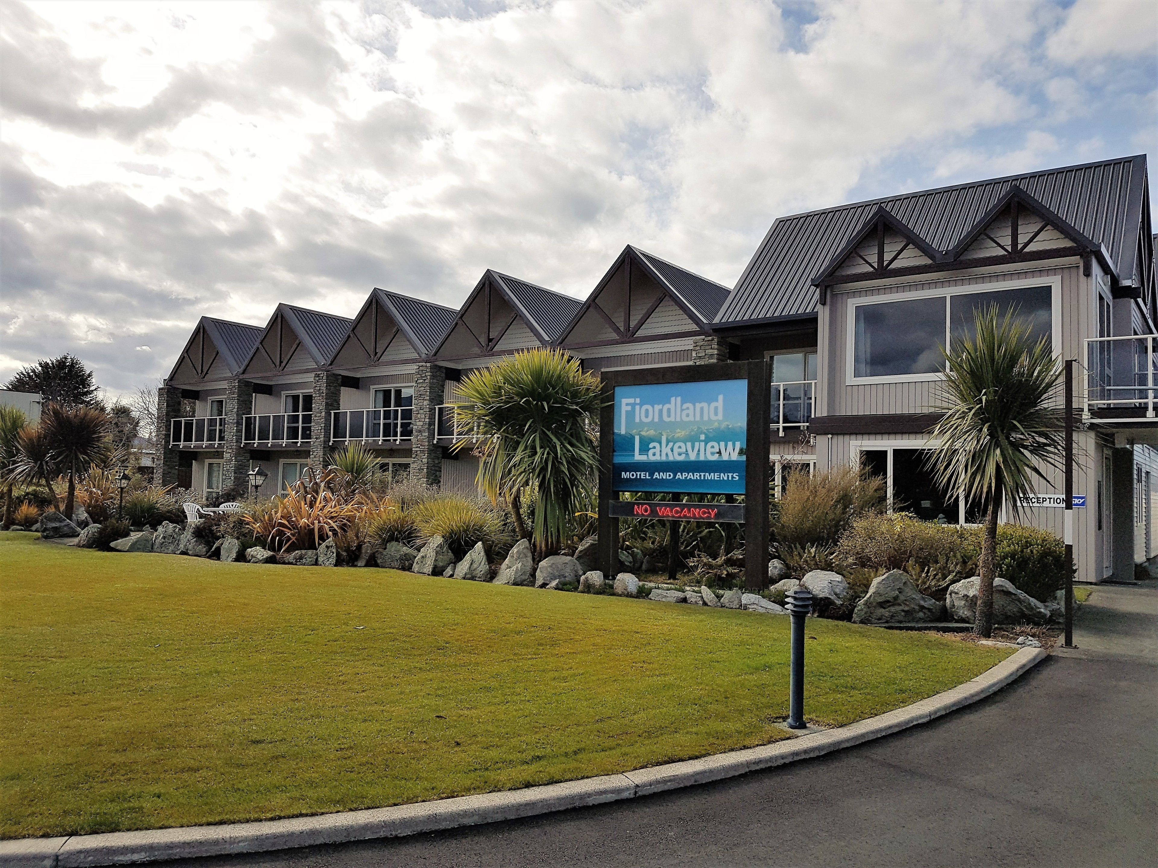 A modern motel and apartments complex named 'Fiordland Lakeview' with a sign indicating no vacancies.