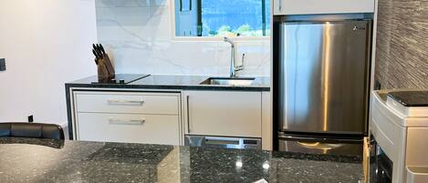 A modern kitchen with a stainless steel refrigerator, a built-in oven, and a granite countertop.