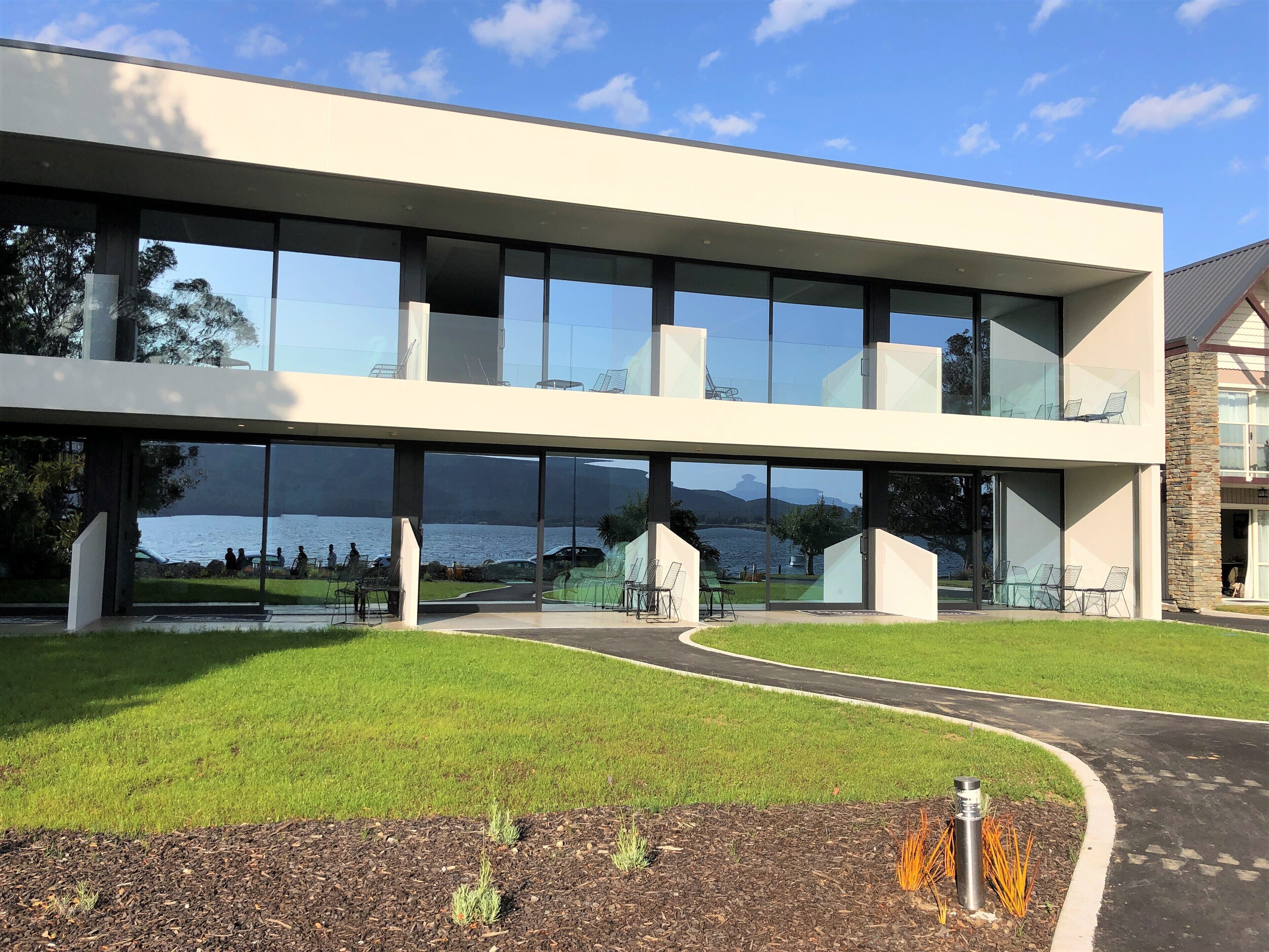 A modern building with large glass windows, a flat roof, and a view of a lake.