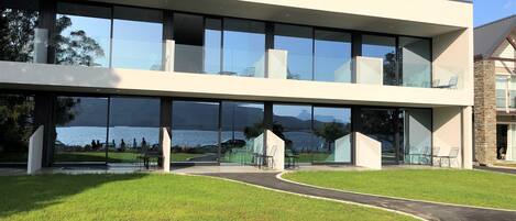 A modern building with large glass windows, a flat roof, and a view of a lake.