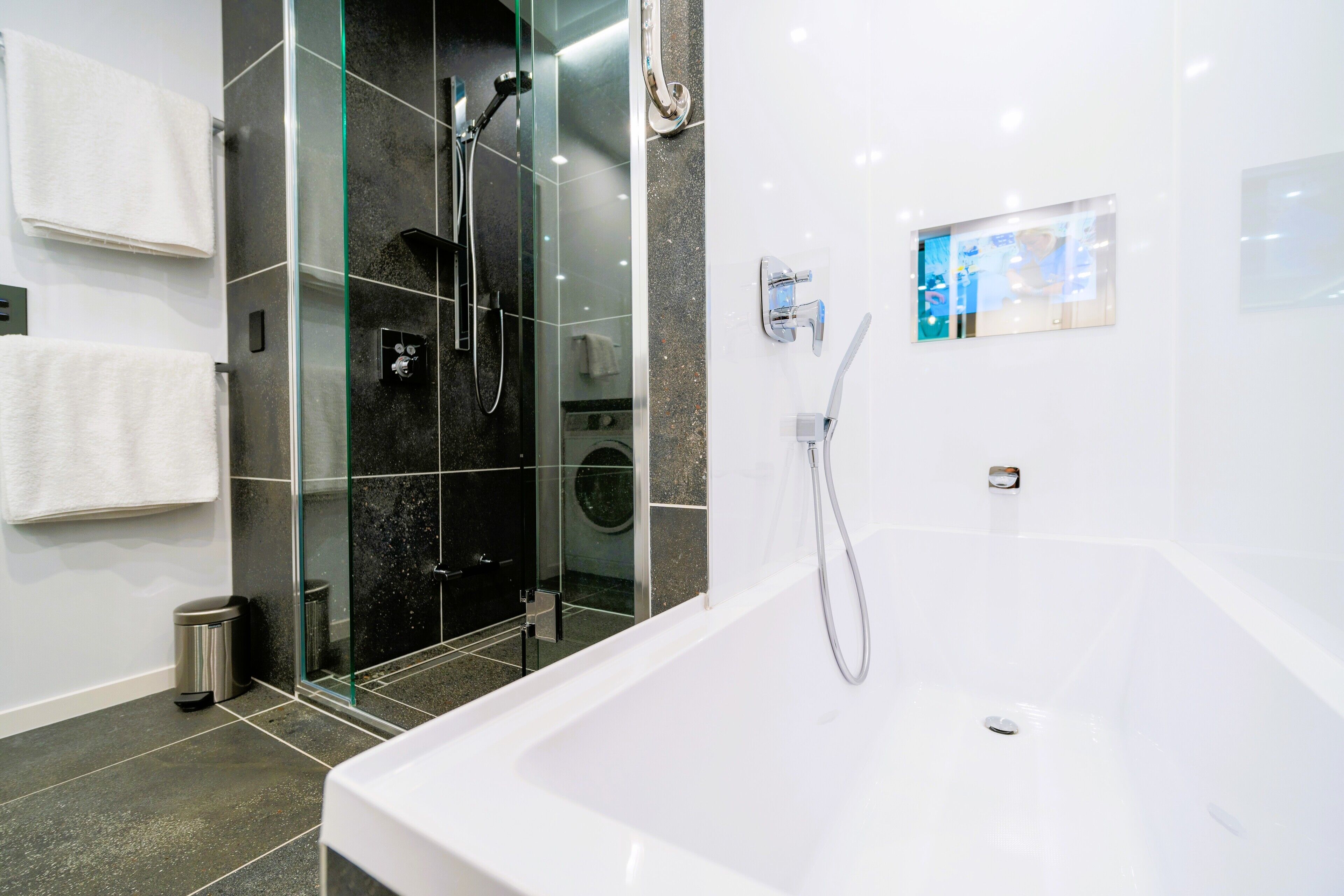 A modern bathroom with a glass-enclosed shower, a standalone bathtub, and a built-in washing machine.