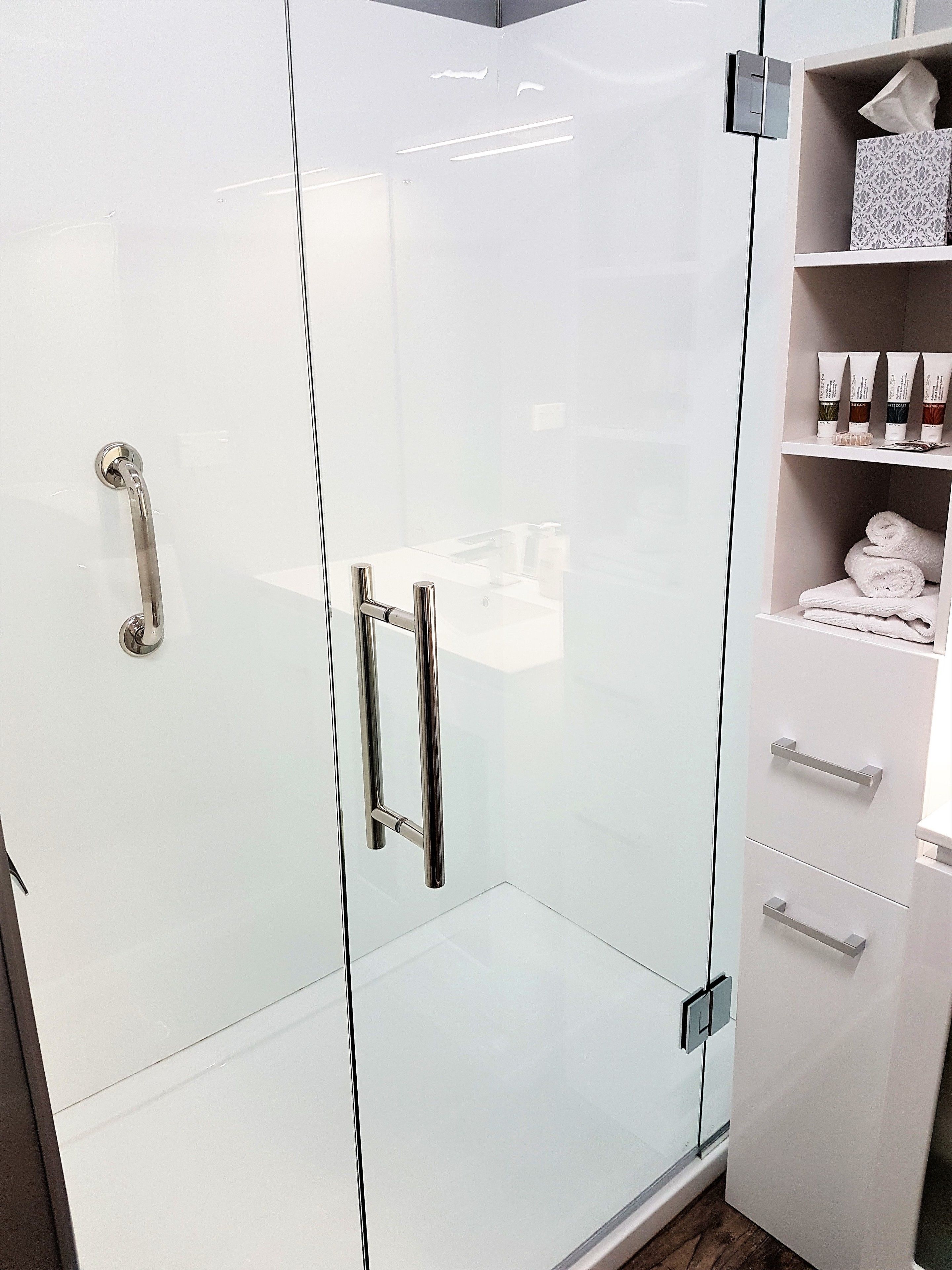 A modern bathroom with a glass shower enclosure, a white vanity with a towel rack, and toiletries on the shelf.