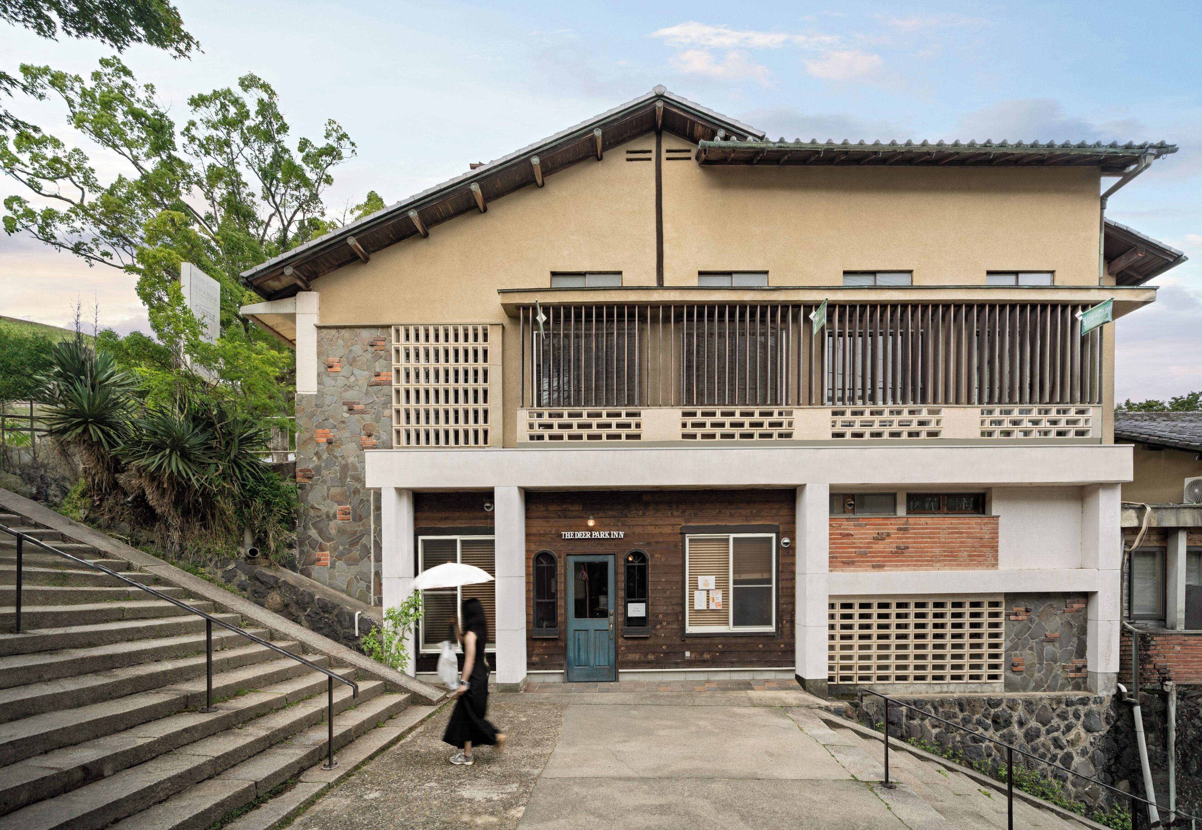A two-story building with a stone facade, a balcony with metal railings, and a staircase leading to the entrance.