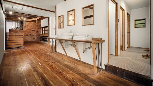 Une pièce au plancher de bois, dotée d’un grand évier, de poutres apparentes et d’un miroir.