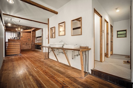 A wooden-floored room with a large sink, wooden beams, and a mirror.