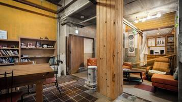 A room with a wooden table, chairs, a bookshelf, a trash bin, and a sofa.